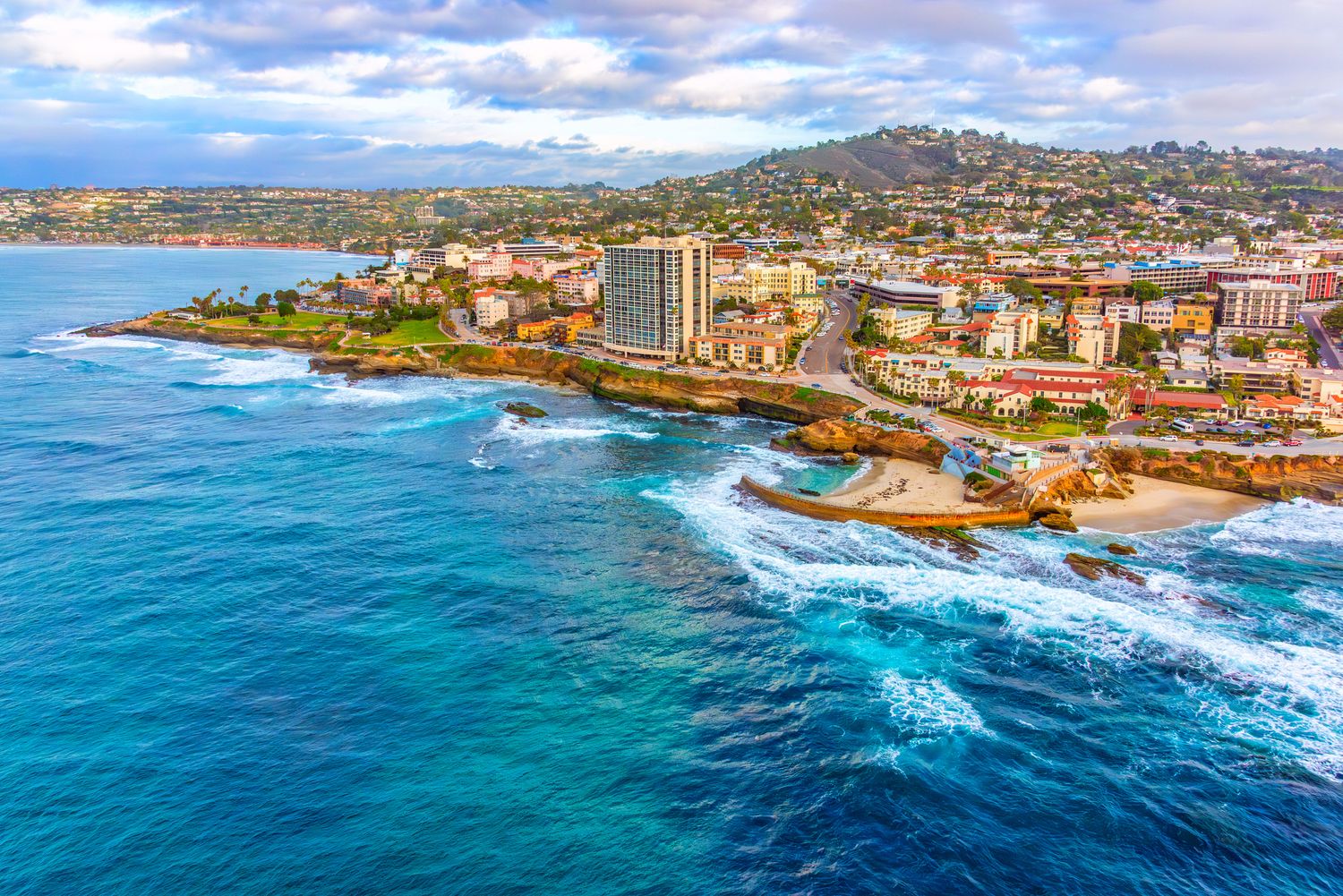 Coastal cityscape with waves and hillside backdrop.