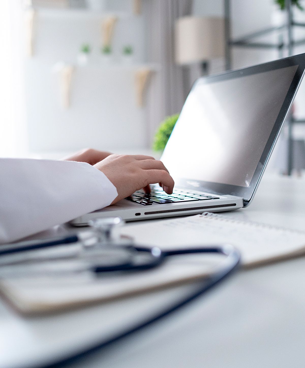 Person typing on laptop with stethoscope nearby.