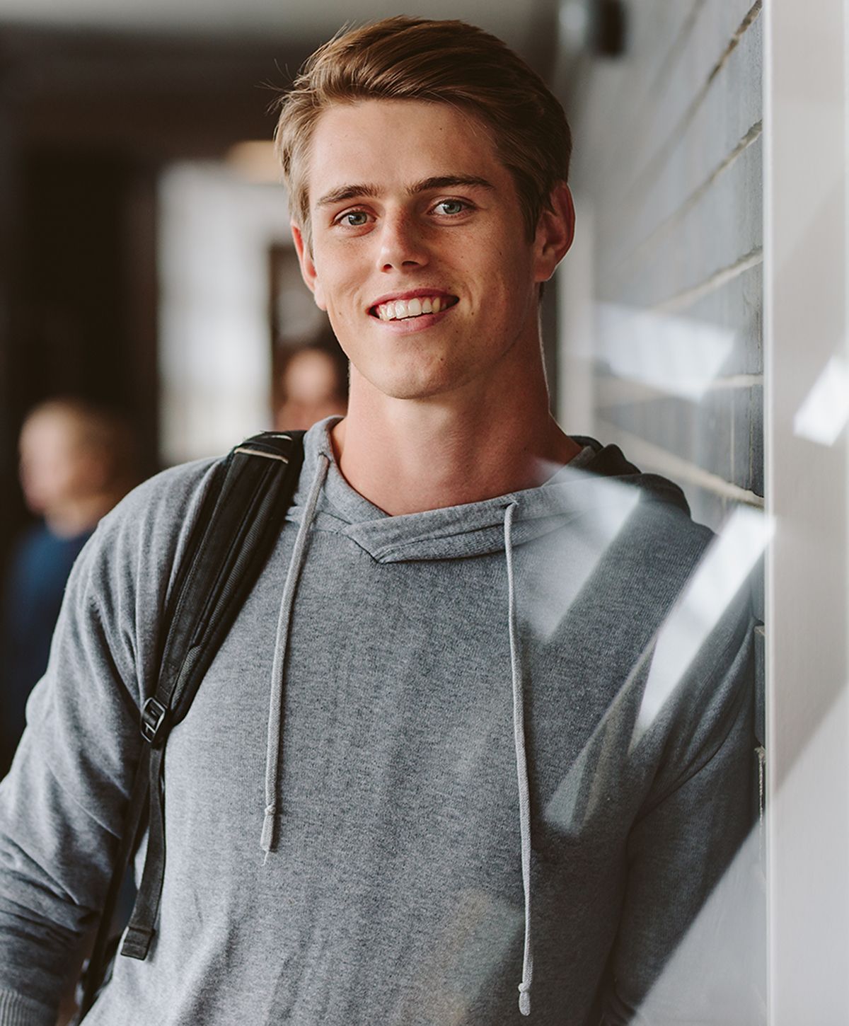 Smiling young man in gray hoodie, indoors.